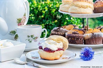 Gedeckter Tisch mit Teekanne, Tasse, Scones und einer Etagere mit Gebäck