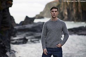 Ein männliches Model trägt einen steingrauen Strickpullover von Fisherman out of Ireland.