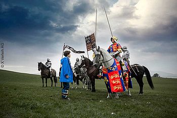 Harry Lloyd und andere Männer sitzen als Ritter kostümiert auf Pferden, die auf einer Wiese Sally Hawkins treffen