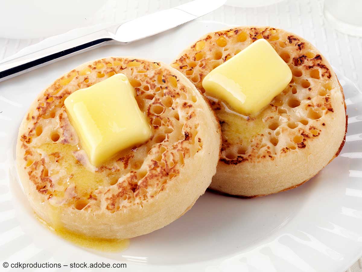 Zwei frisch gebackene Crumpets, auf denen Butterstückchen zerlaufen.